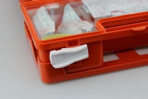 Close-up of an orange plastic Dog first aid kit with a white latch, showing medical supplies like bandages and dressings inside the partially open container—essential for adventure dogs in remote locations.