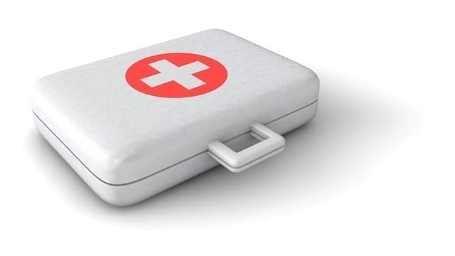 A white first aid kit with a red circle and white cross on the lid, resting on a white surface—perfect for hiking with your dog.